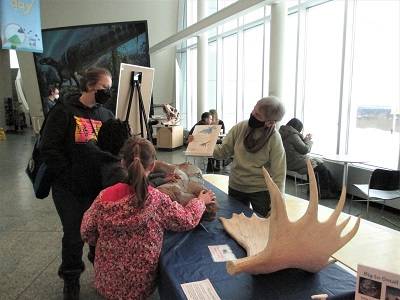 Children look at a replica dino bone and moose antler on a table.