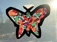 Butterfly-shaped suncatcher made with tissue paper pieces, with sunlight shining through.