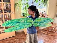 Child modeling cardboard wings painted to look like dragonfly wings, seen from the back.