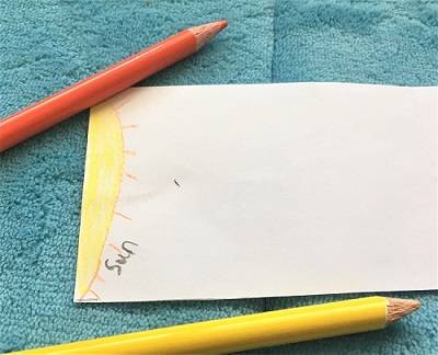 White piece of paper with the sun drawn on one edge. Two colored pencils are next to the paper.