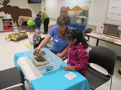 Geologist Jaenell Manchester helps a young visitor pan for gold in a plastic bin.