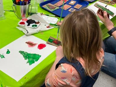 Child making art with rodent-shaped foam stamps and paint.