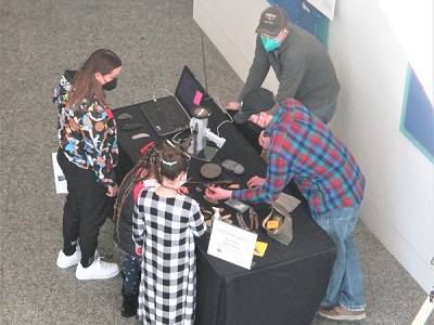 Several visitors looking at tools on a table in the museum lobby.
