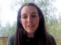 Person with long dark hair looking at the camera, with trees in the background.