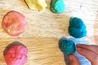 Hand arranging balls of colored play dough in a circle to represent a color wheel.
