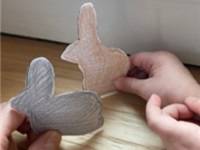 Child's hand holding two snowshoe hare cutouts, one brown and one gray.