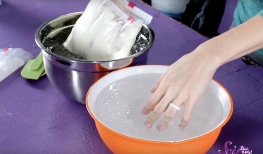 Two hands in bowls of ice water. One hand is bare, and the other is in a Ziploc bag full of shortening.
