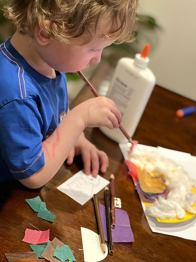 A child holds a colored pencil and works on a collage.