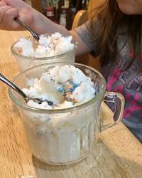 Dish of white ice cream with multicolored sprinkles on top. A child's hands are in the background.