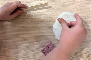 Child's hands using a popsticle stick and a piece of plastic netting to make marks on a piece of clay.