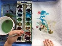 Hand holding a paintbrush and painting a paper towel.