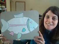 Person holding a piece of cardboard with a paper outline of a fish glued on it.