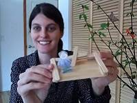 Person sitting next to a bouquet of green branches, and holding a toy boat.