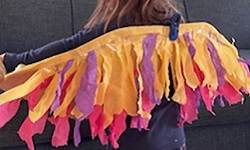 Child wearing a cardboard pair of wigs decorated with yellow, purple, and pink streamers.