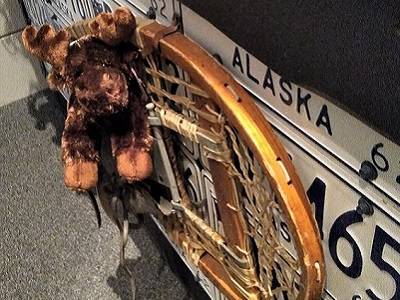 Moose plushie next to a snowshoe mounted on a wall of Alaska license plates.