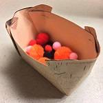 Model birch basket, with birch-patterned paper visible on the outside. The basket is half-filled with pom-poms in different colors.