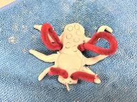 Clay sculpture of a beetle, with wings and antennae made from red pipecleaners and a proboscis made from a toothpick.