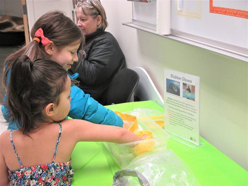 Two children dipping their hands in a tub of ice water, with shortening to insulate their hands. An adult sits in the background.
