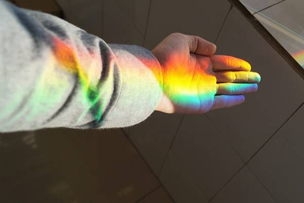 Sunlight separated into rainbow colors, shining on a child's hand.