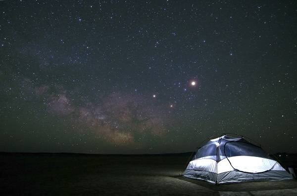A tent set up in a field, with a starry sky in the background.