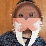 Person wearing a walrus mask made from a paper plate, tissue paper, and construction paper.