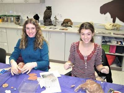 Two teenagers sit at a table working on a faux taxidermy project.