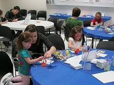 An adult and two children sit at a table, working on an art project.