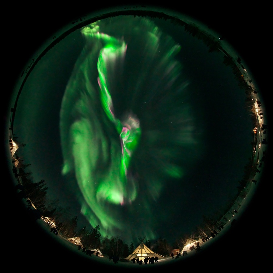 Fisheye view of aurora over lit up tents