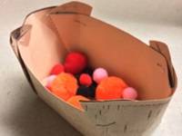 Model birch basket, with birch-patterned paper visible on the outside. The basket is half-filled with pom-poms in different colors.