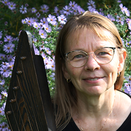Arja Kastinen poses with her kantele in front of blue flowers