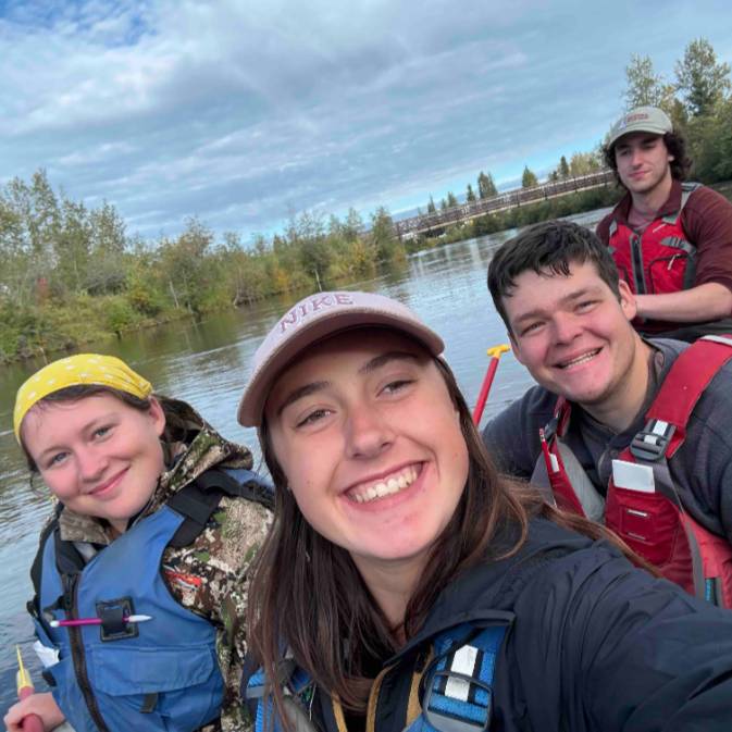 Inga, foreground, takes a selfie with 3 friends in the background. They are in a raft on a river.