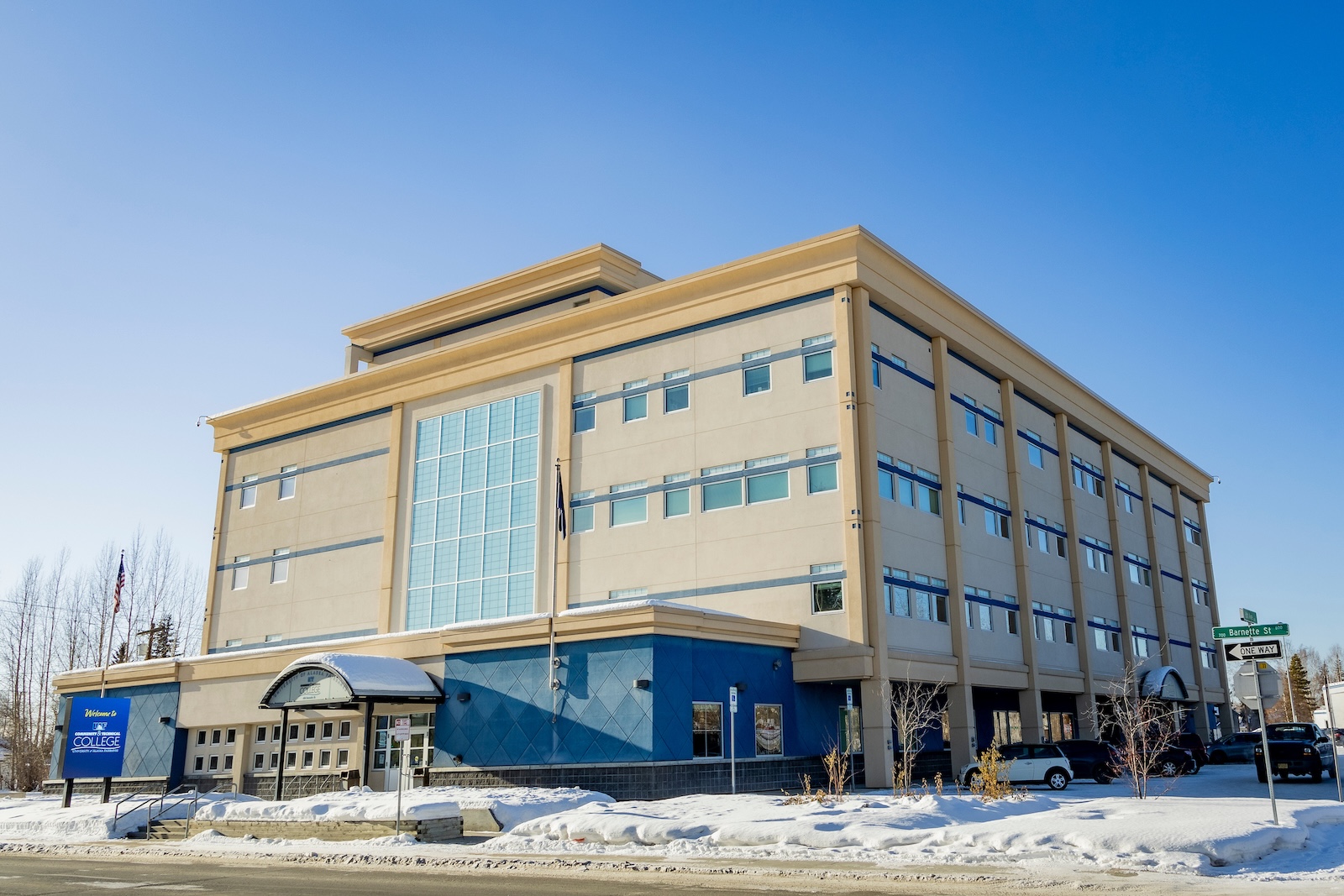 A large, square four-story building housing the UAF Community and Technical College and painted beige with blue trim on a snowy street.