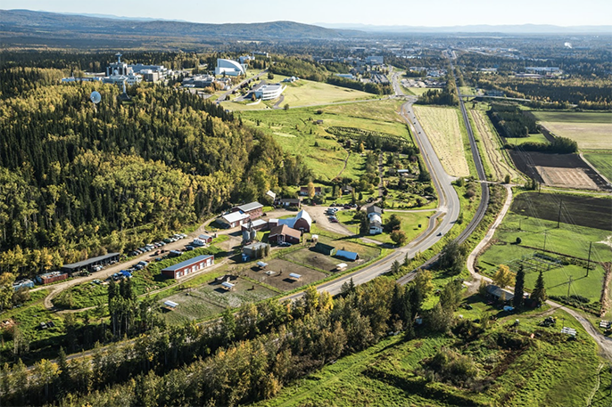 An aerial view of a green hillside with farm buildings, fields and gardens