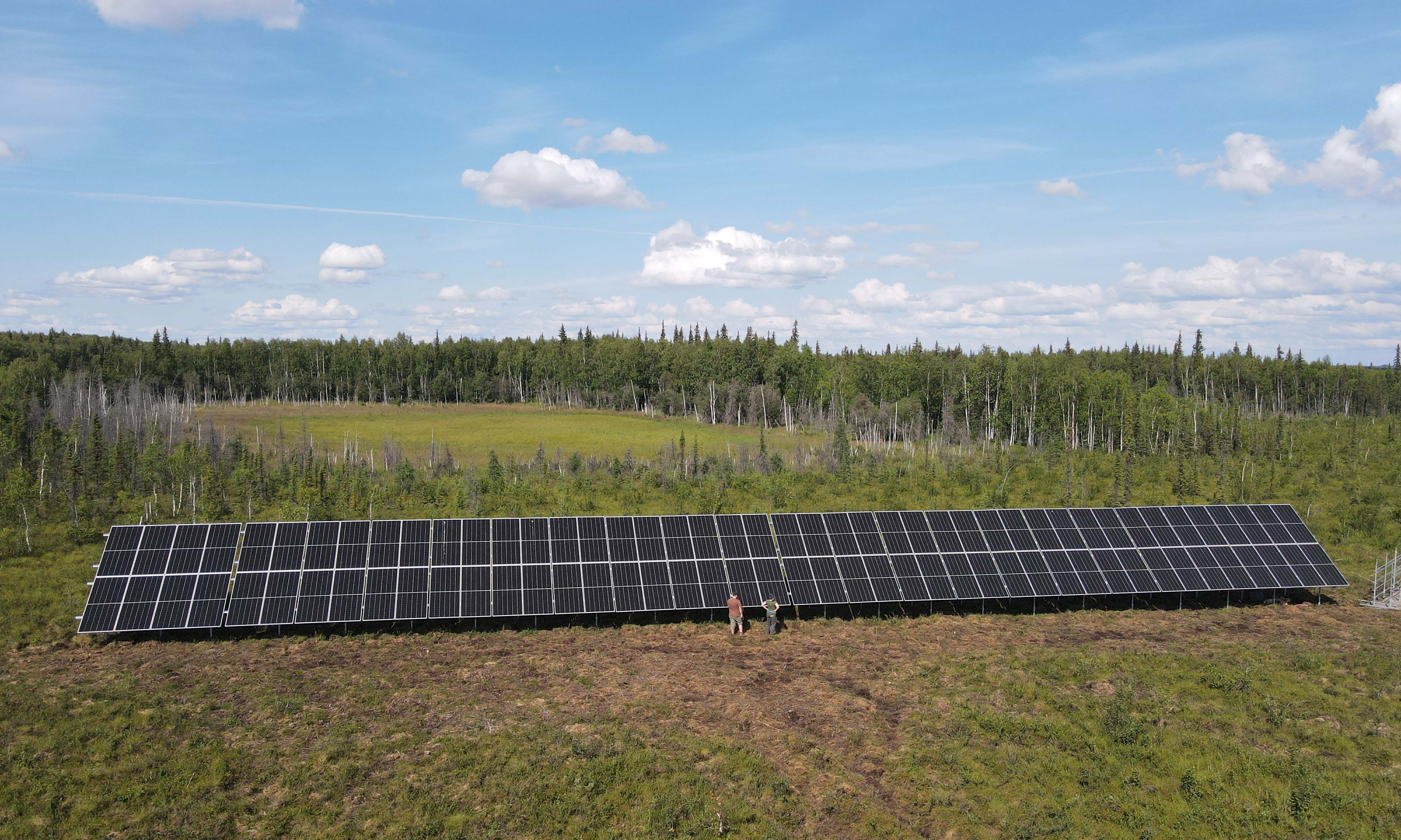 Two people stand in front of a solar array