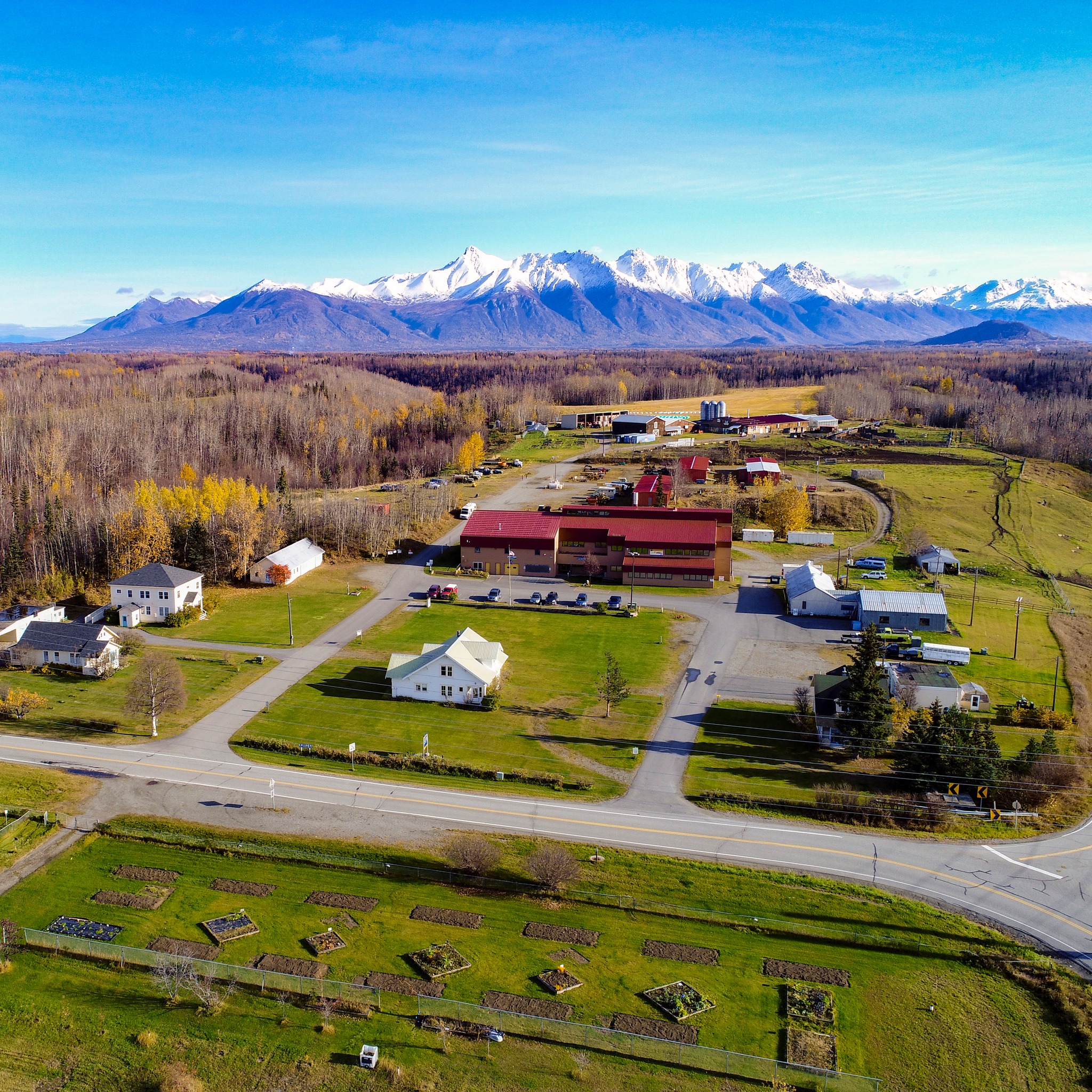 An aerial view of gardens, barns and other farm buildings with snow-capped mountains in the background.