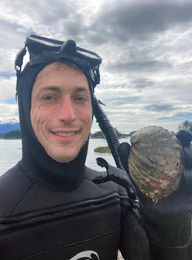 A man in a wetsuit holds up an round abalone 