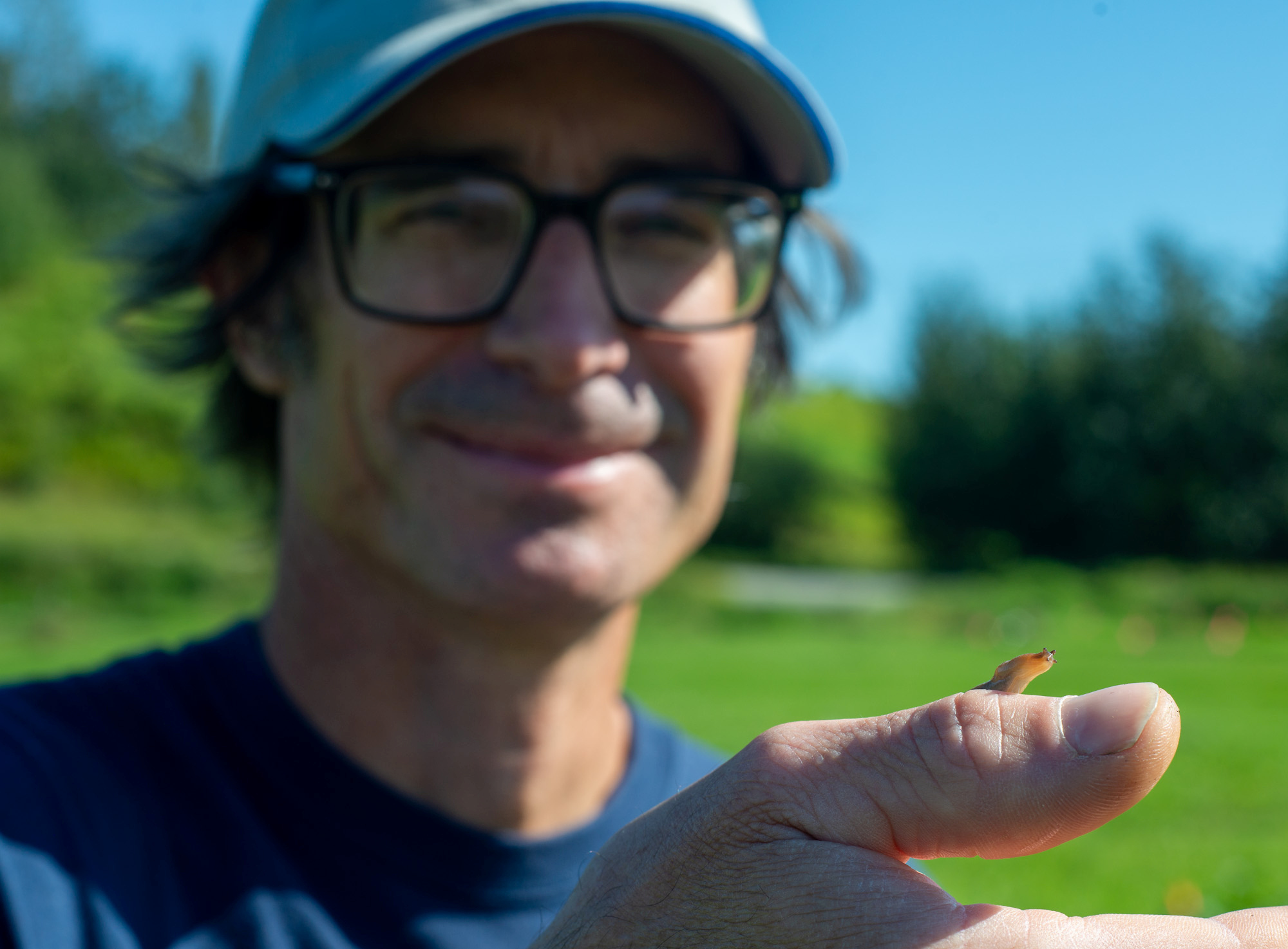 A smiling man extends a hand with a slug peeking over his fingers
