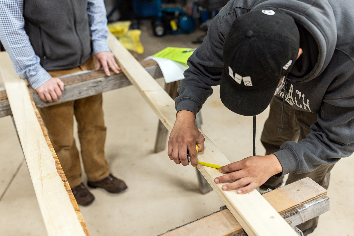 A person in a lumber grading training class measures a defect on a board propped up on sawhorses