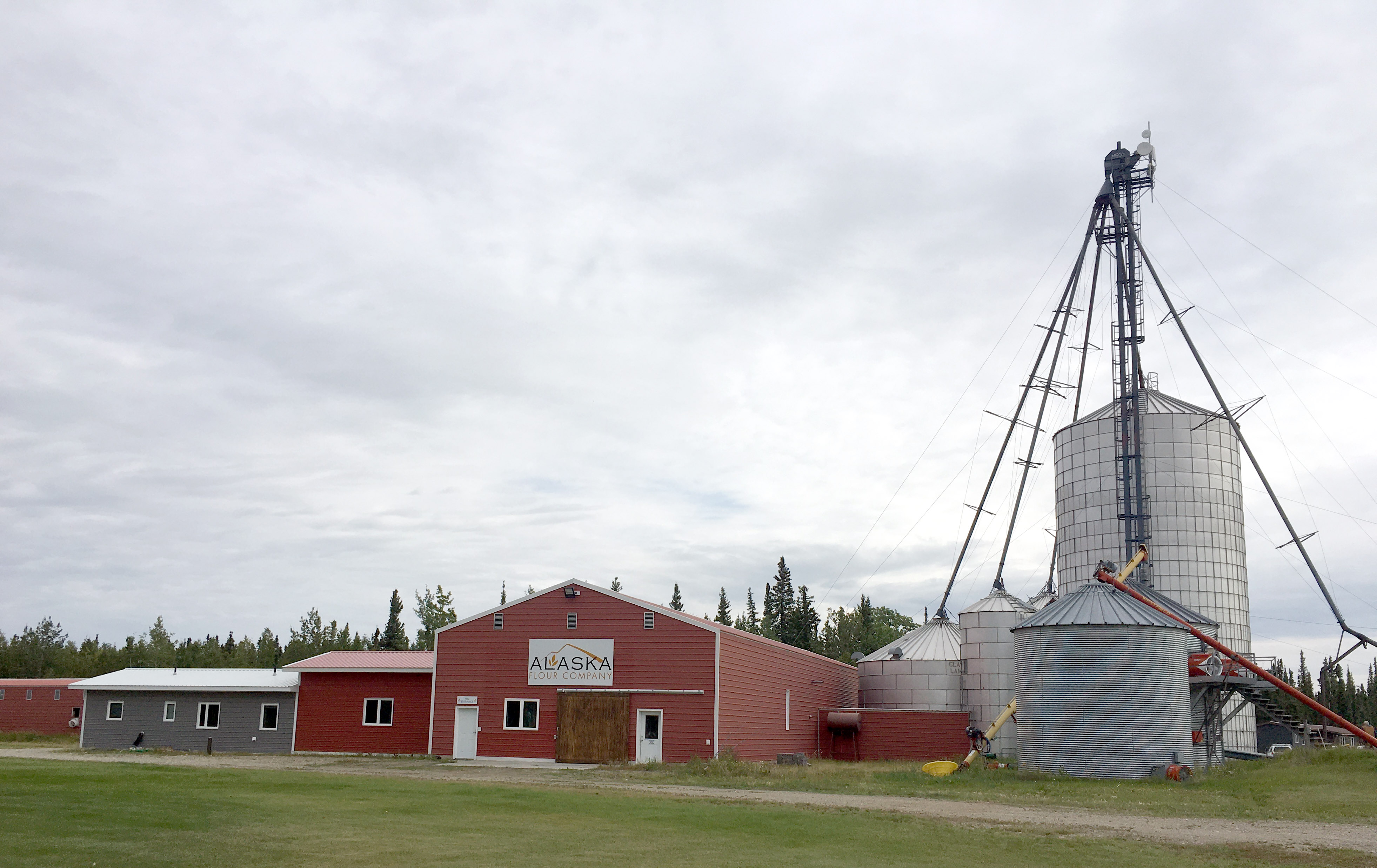 A grain silo is next to a group of red-painted agriculture processing buildings