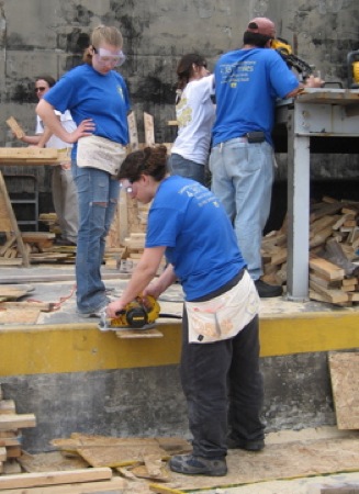Cynthia Lashinski holds the board for Clarissa Ribbens as she operates a saw. In the background Temple Dillard supervises the operation of a chop saw. Photo by Brian Lyke
