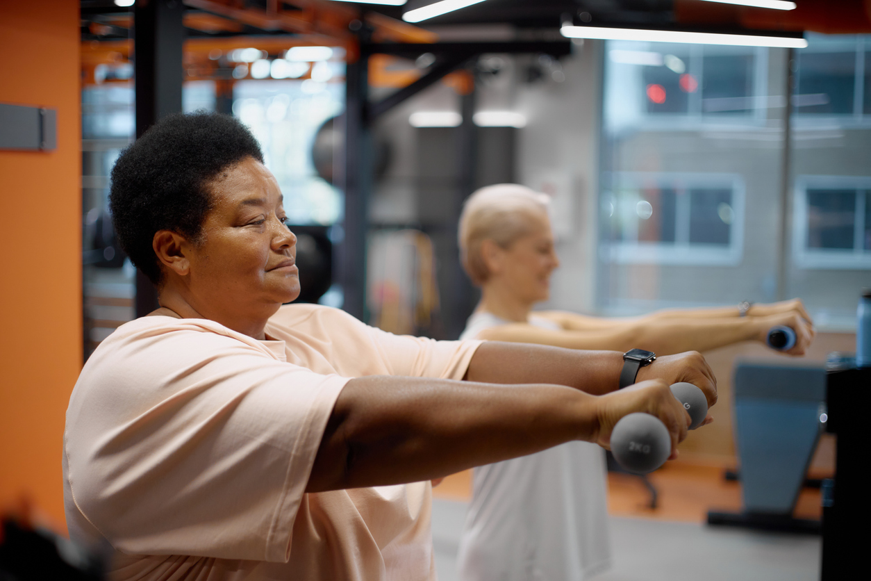 Two women lift hand weights in a gym