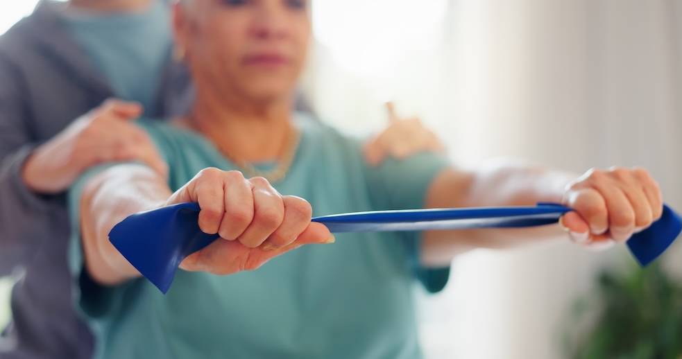A woman pulls on a resistance band with another person behind her to ensure safety