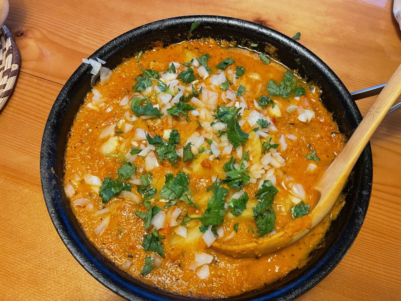 A bowl of yellow potato curry garnished with onions and cilantro in a bowl with a wooden spoon