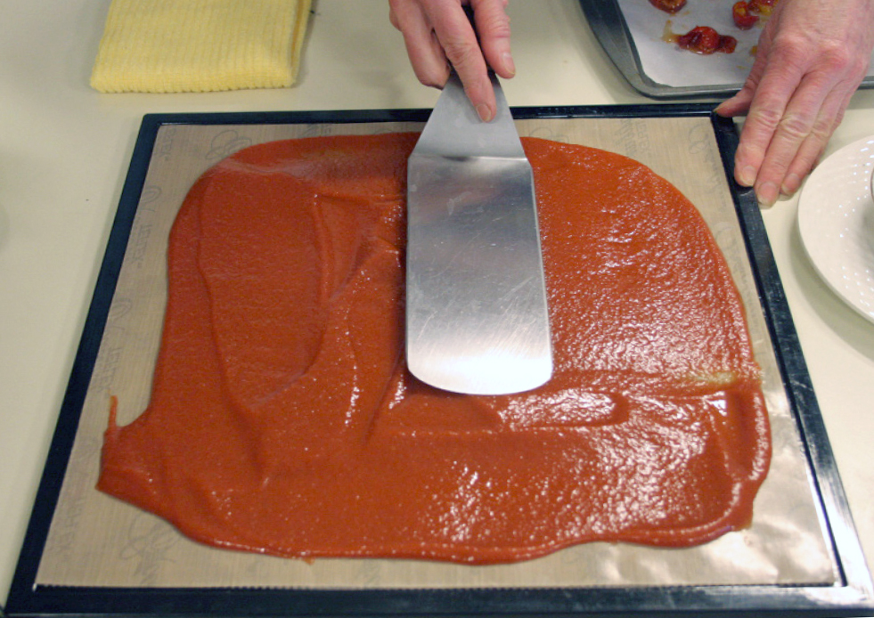 Red fruit puree is spread across a pan with a silver spatula.