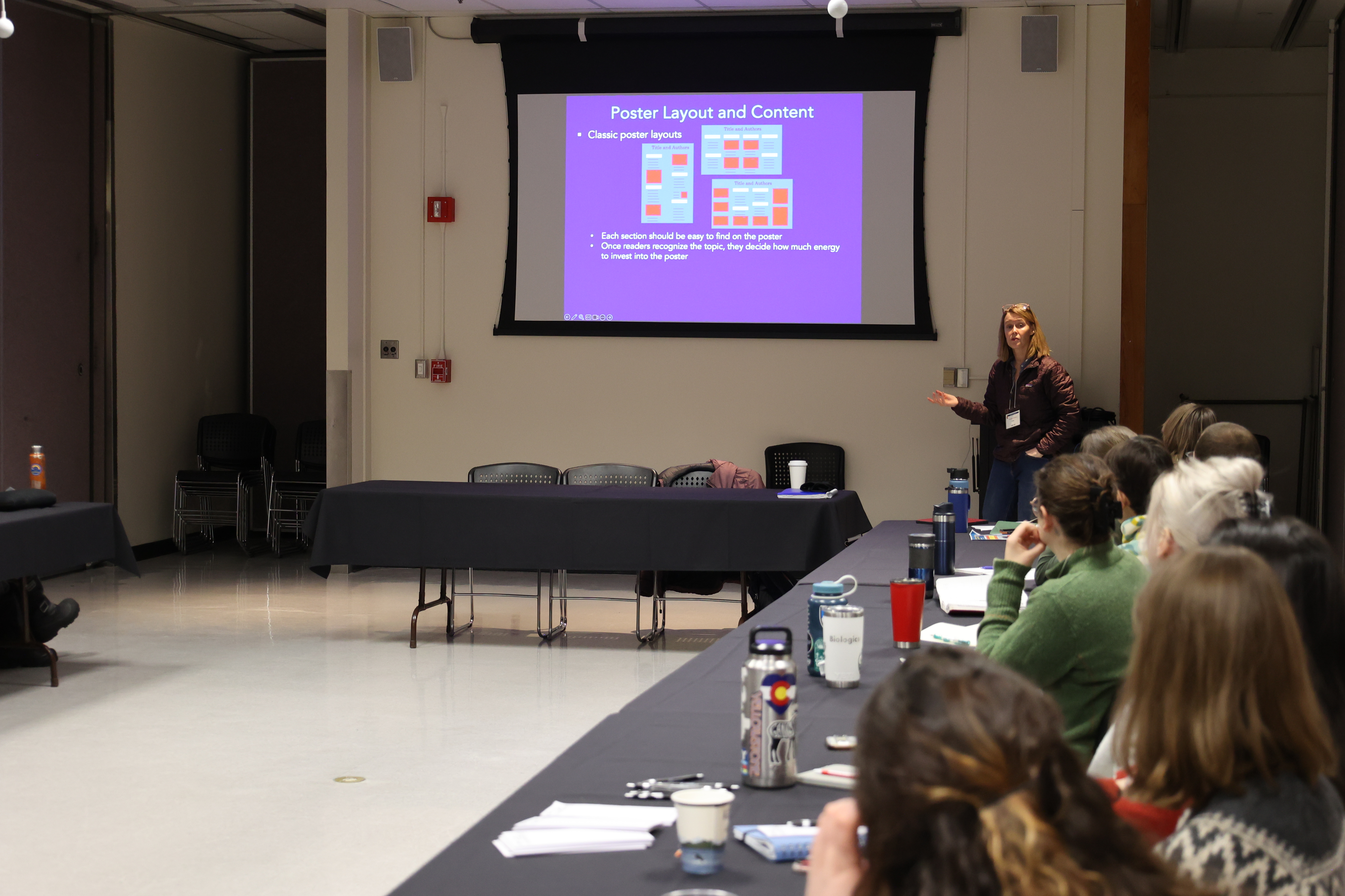 Kristen Gorman presents to students in a conference room. She stands beside a projector screen with a slide titled, 