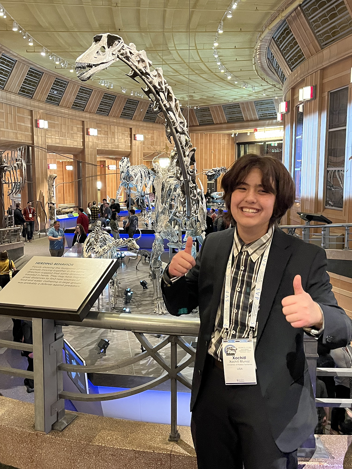 person standing in front of dinosaur fossils with thumbs up