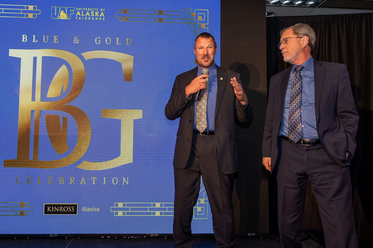 UAF alumnus Glenn Brady '93 (left) takes the microphone alongside Geophysical Institute Director Bob McCoy (right) during the experience auction at the 2026 Blue & Gold Celebration.