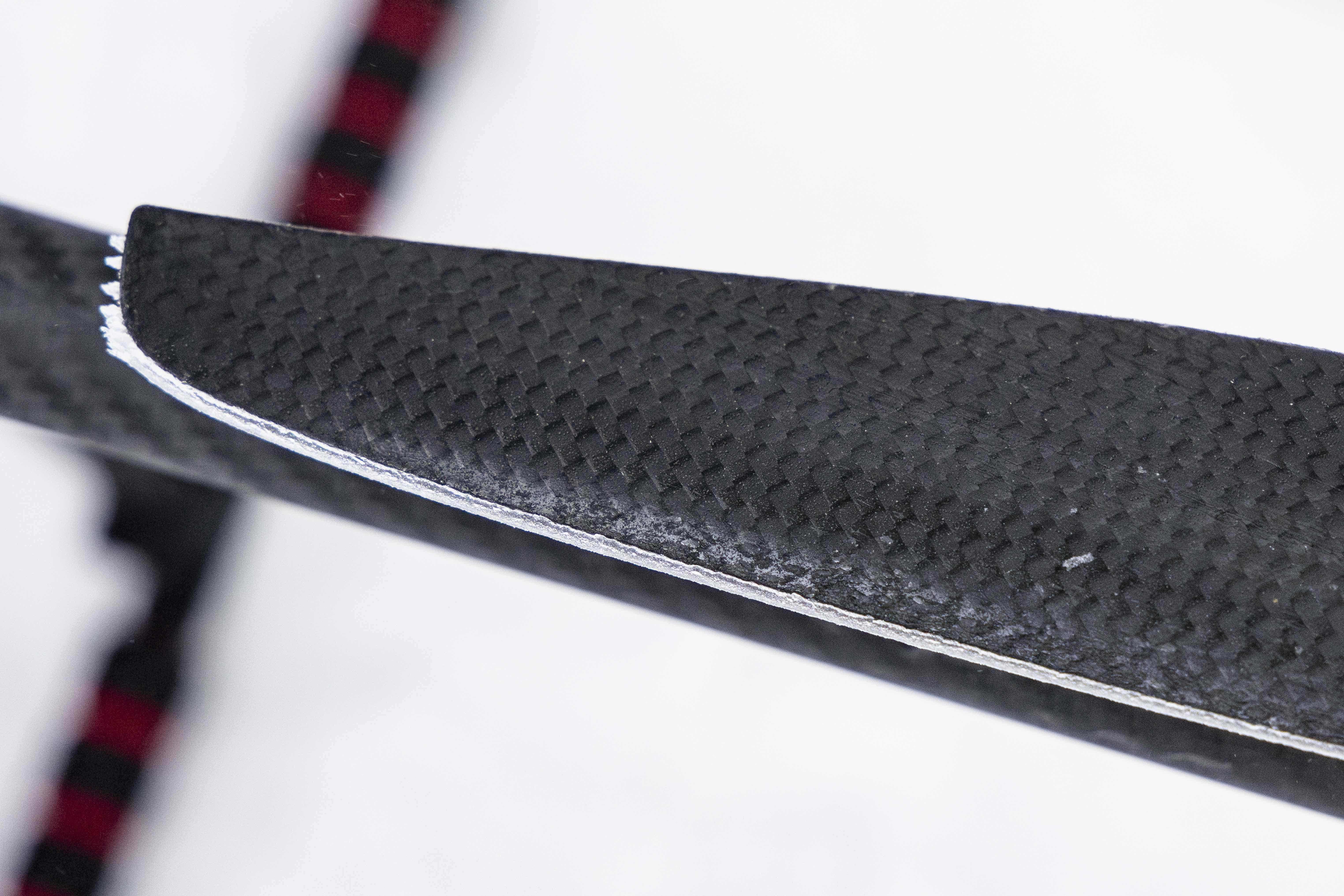 Close-up of ice buildup along the leading edge of a black carbon-fiber drone rotor blade. A thin white ridge of ice traces the blade’s edge against a white background.