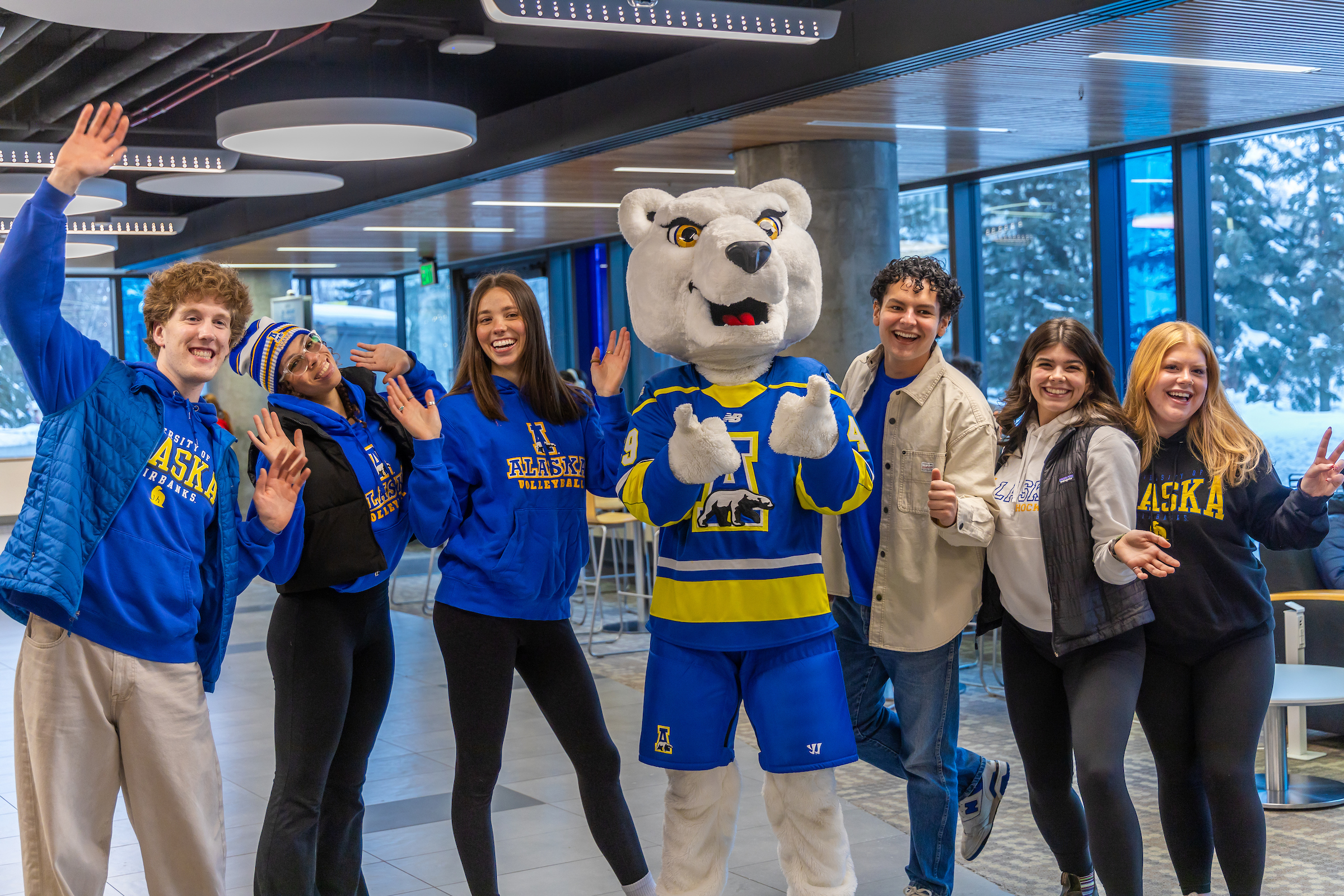 Six smiling people wearing UAF clothing stand, three on each side, next to a polar bear mascot wearing an Alaska Nanooks jersey.