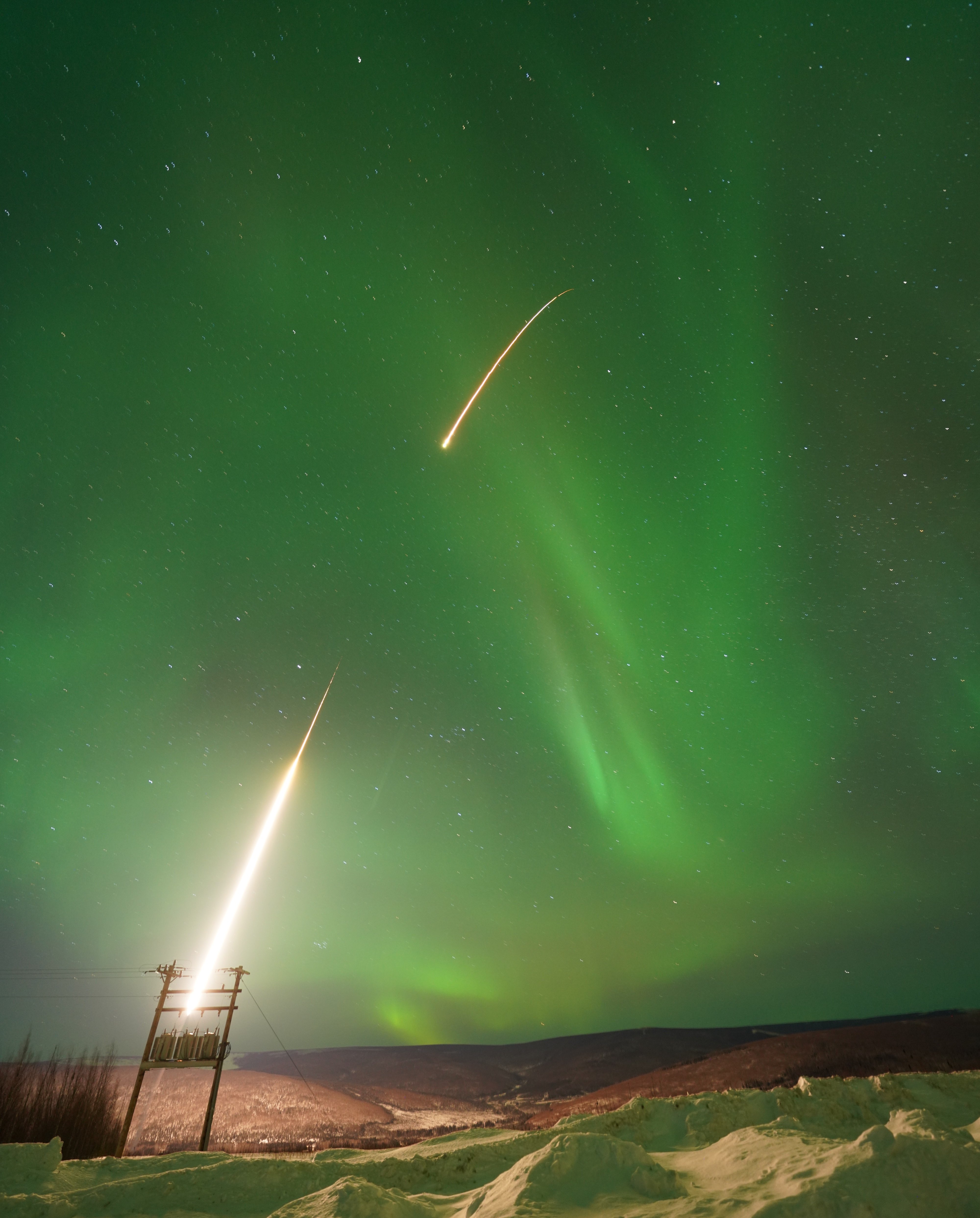 Under a sky filled with green northern lights and stars, a second NASA sounding rocket launches from Poker Flat Research Range around 3:30 a.m., its brilliant plume rising above snow-covered ground in a mission to investigate black aurora.